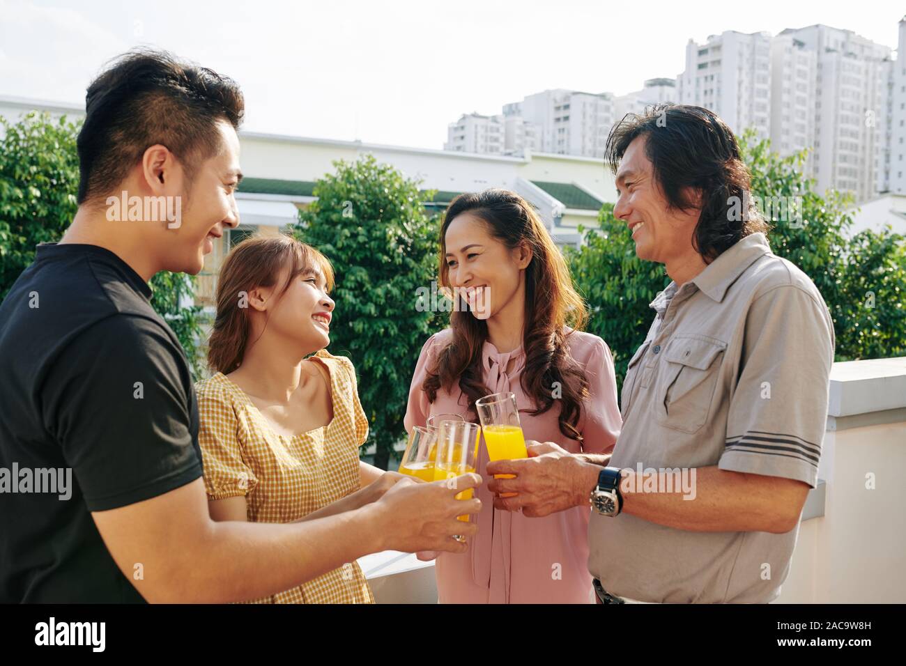 Cheerful middle-aged couple and their adult children drinking juice when having small rooftop party Stock Photo