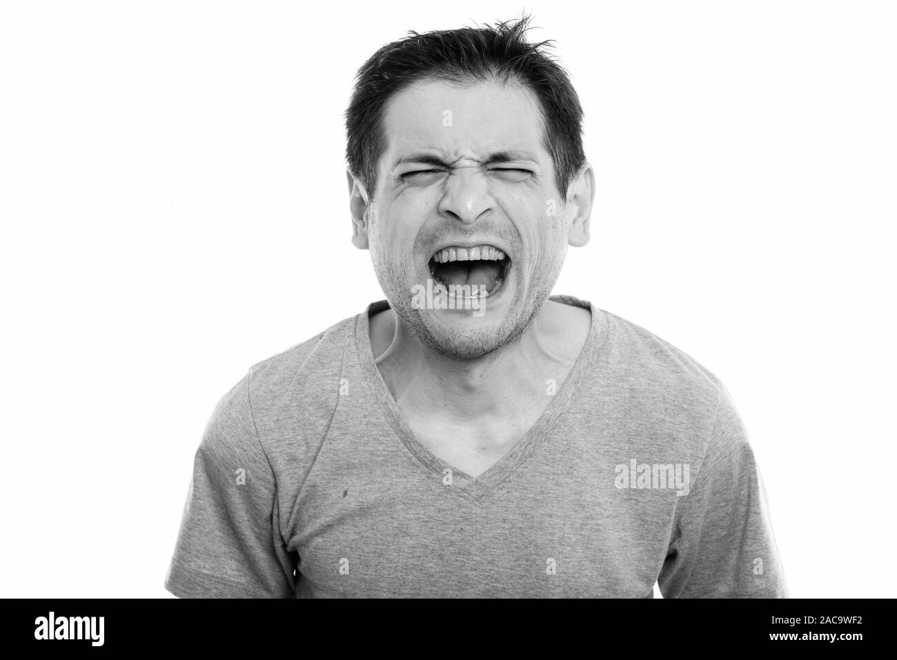 Studio shot of angry young man screaming with eyes closed Stock Photo