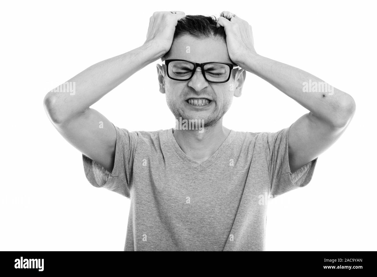 Studio shot of angry young man wearing eyeglasses while pulling his hair Stock Photo