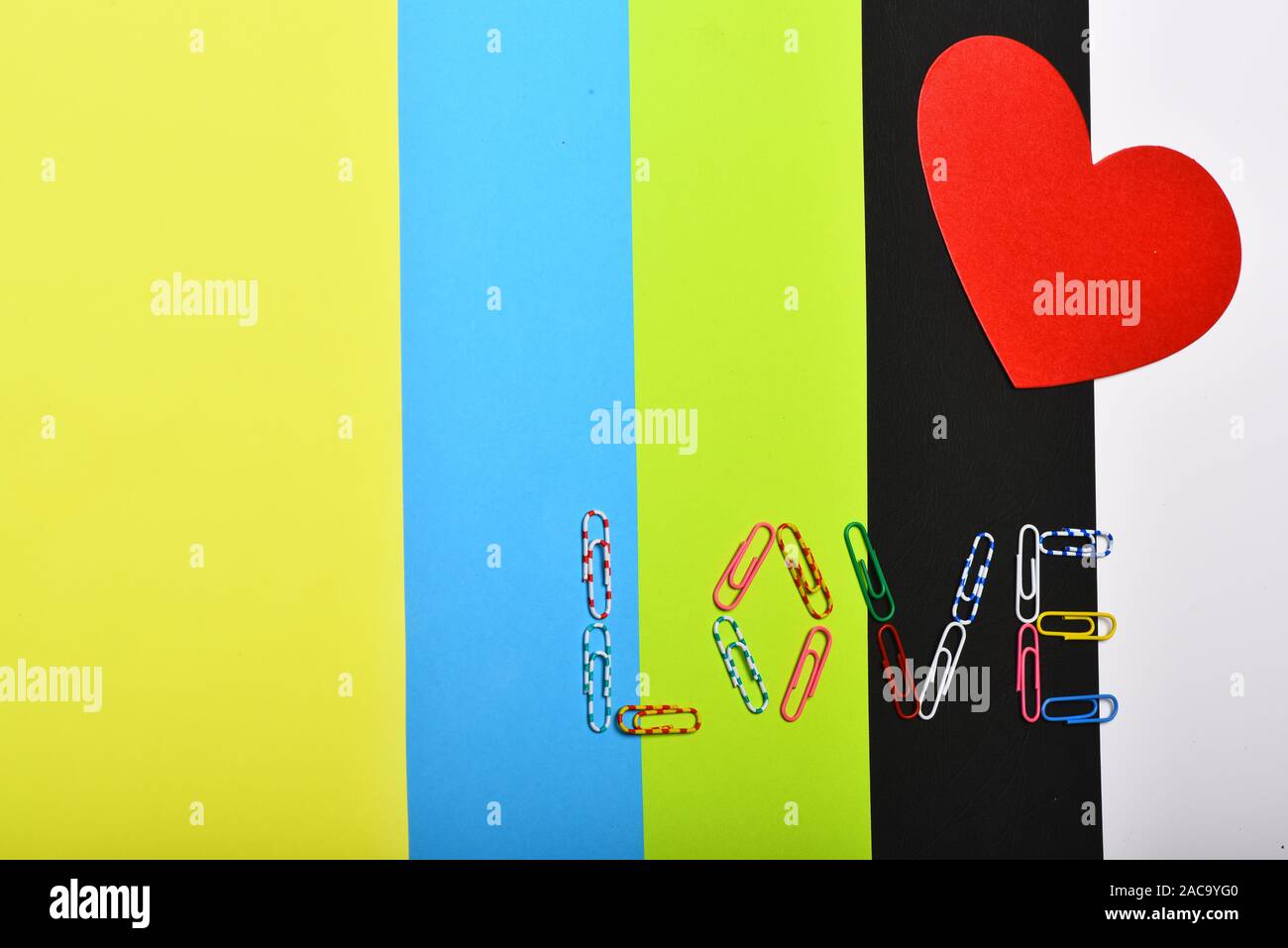 Red paper heart on colourful background, top view. Love and relationship concept. Valentines day card with copy space. Colourful paper clips forming word LOVE. Stock Photo