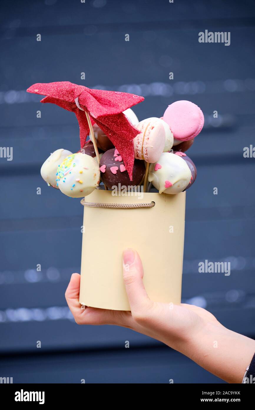 Woman's hand holding and displaying a bouquet made of sweets, macaroon and puff balls on sticks held in vase.  Zagreb, Croatia - November 30, 2019 Stock Photo