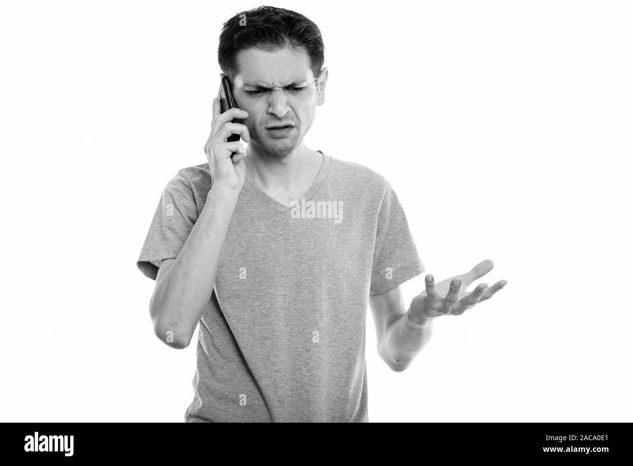 Studio shot of angry young man talking on mobile phone Stock Photo