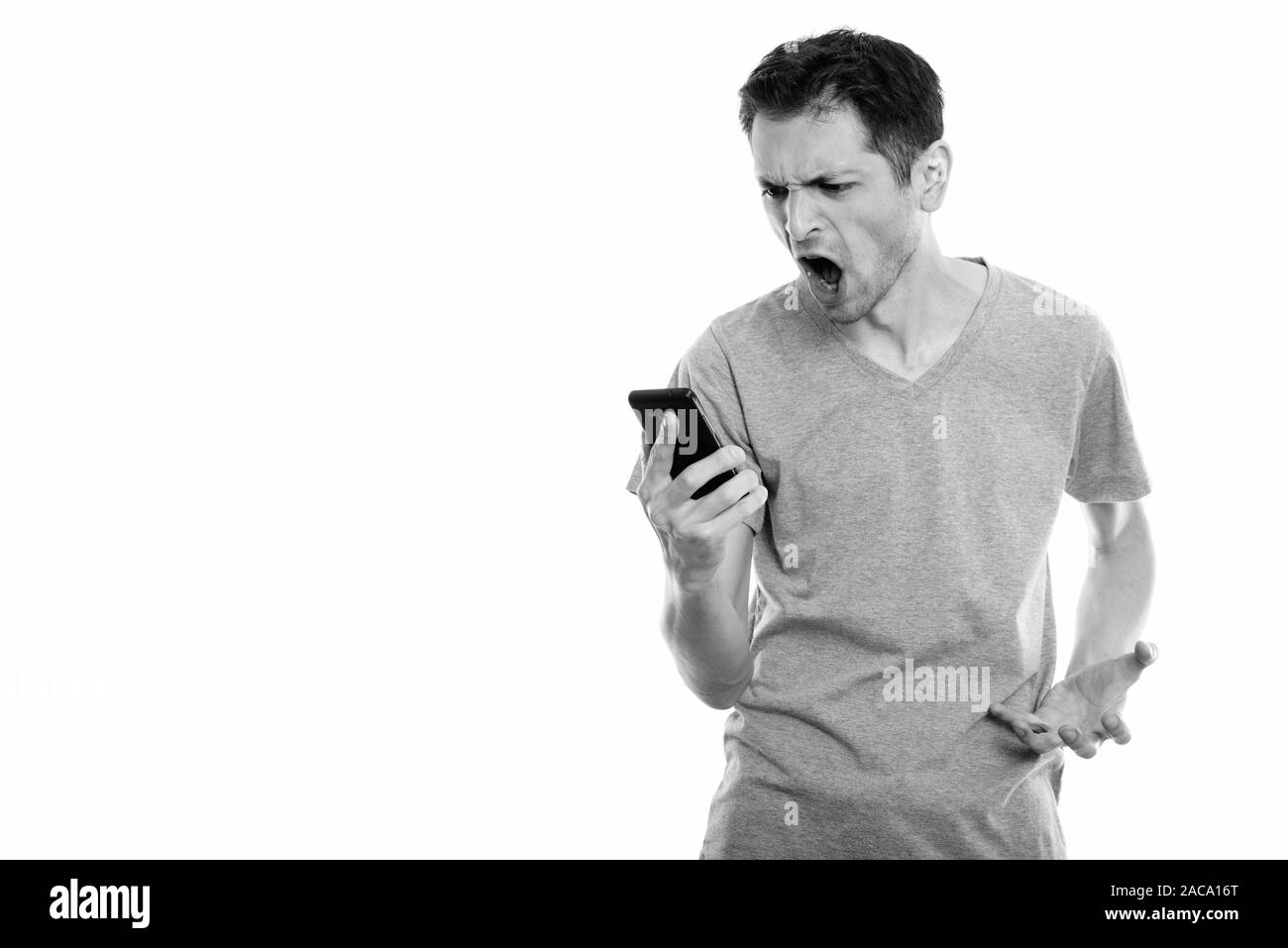 Studio shot of angry young man shouting while using mobile phone Stock Photo
