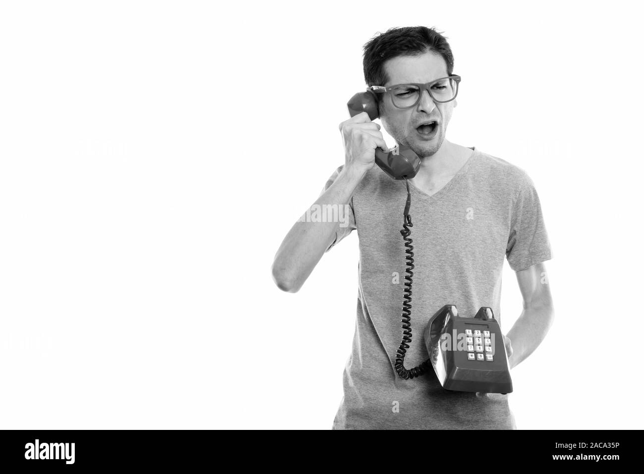 Studio shot of angry young man talking on old telephone Stock Photo