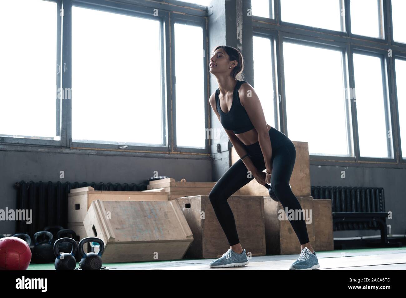 Side view of young beautiful woman with perfect body in sportswear working out with kettle bell at gym. Stock Photo