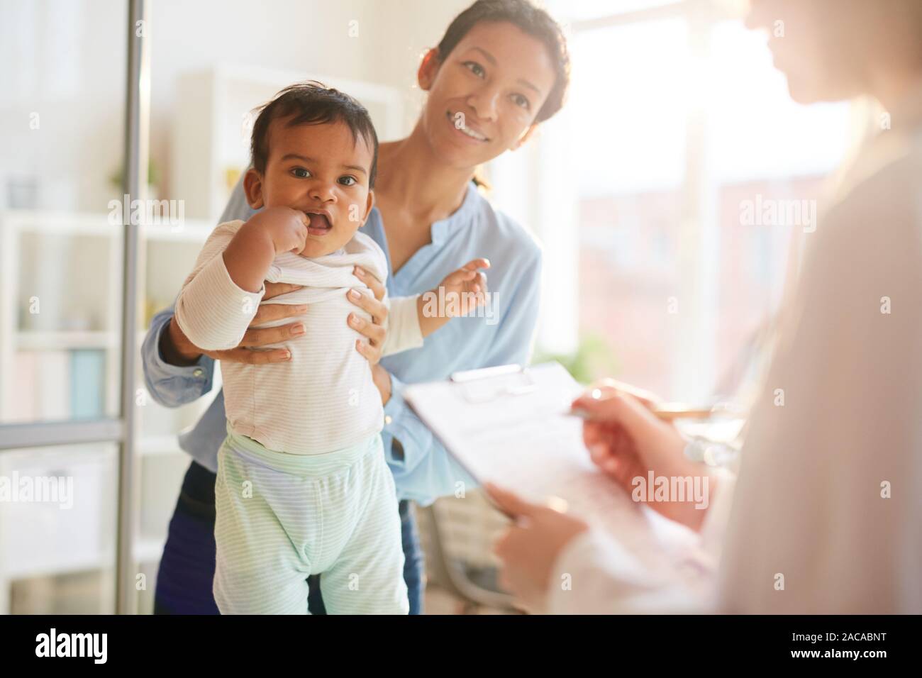 Happy young mother with little child smiling and talking to the pediatrician during medical exam at hospital Stock Photo