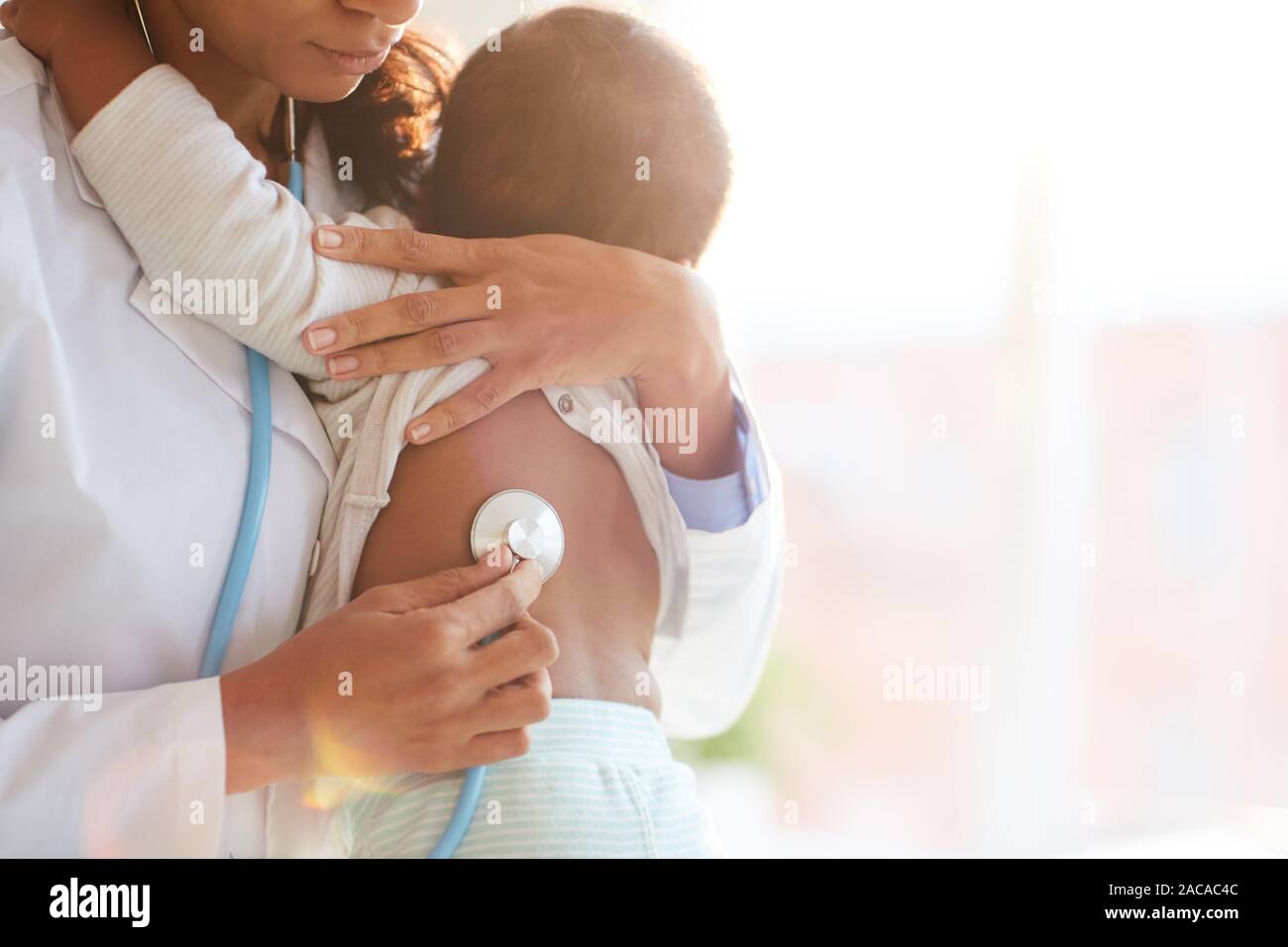 Doctor holding baby and listening to him with stethoscope Stock Photo