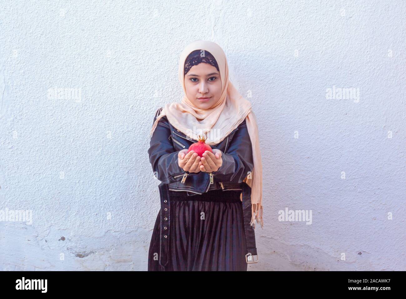 Beautiful middle-eastern girl holding pomegranate fruit. Cute Arabian Muslim woman received unique present - exotic fruit pomegranate Stock Photo