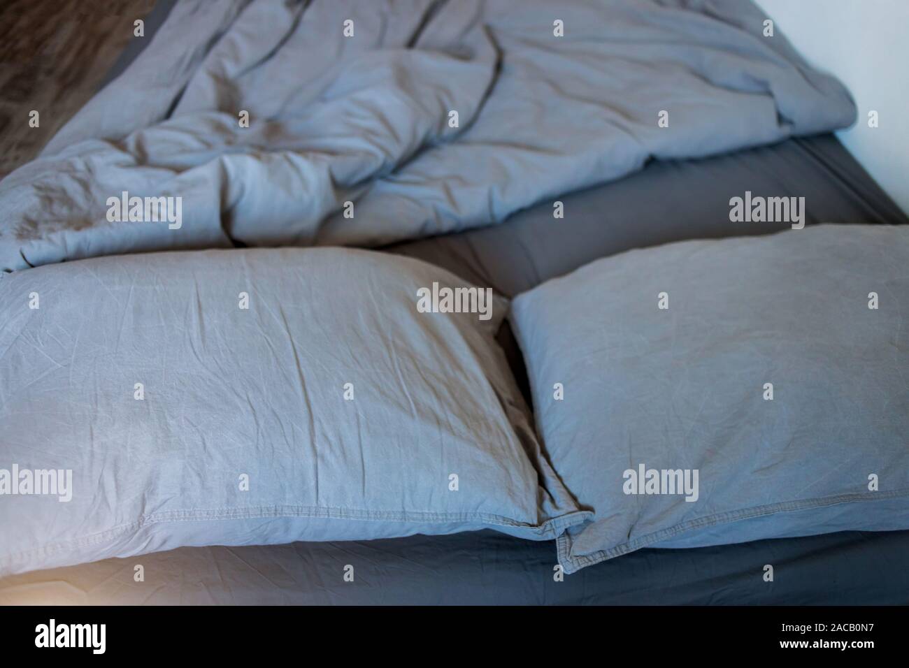 Closeup of gray pillows and blankets with a sheet on the bed Stock Photo