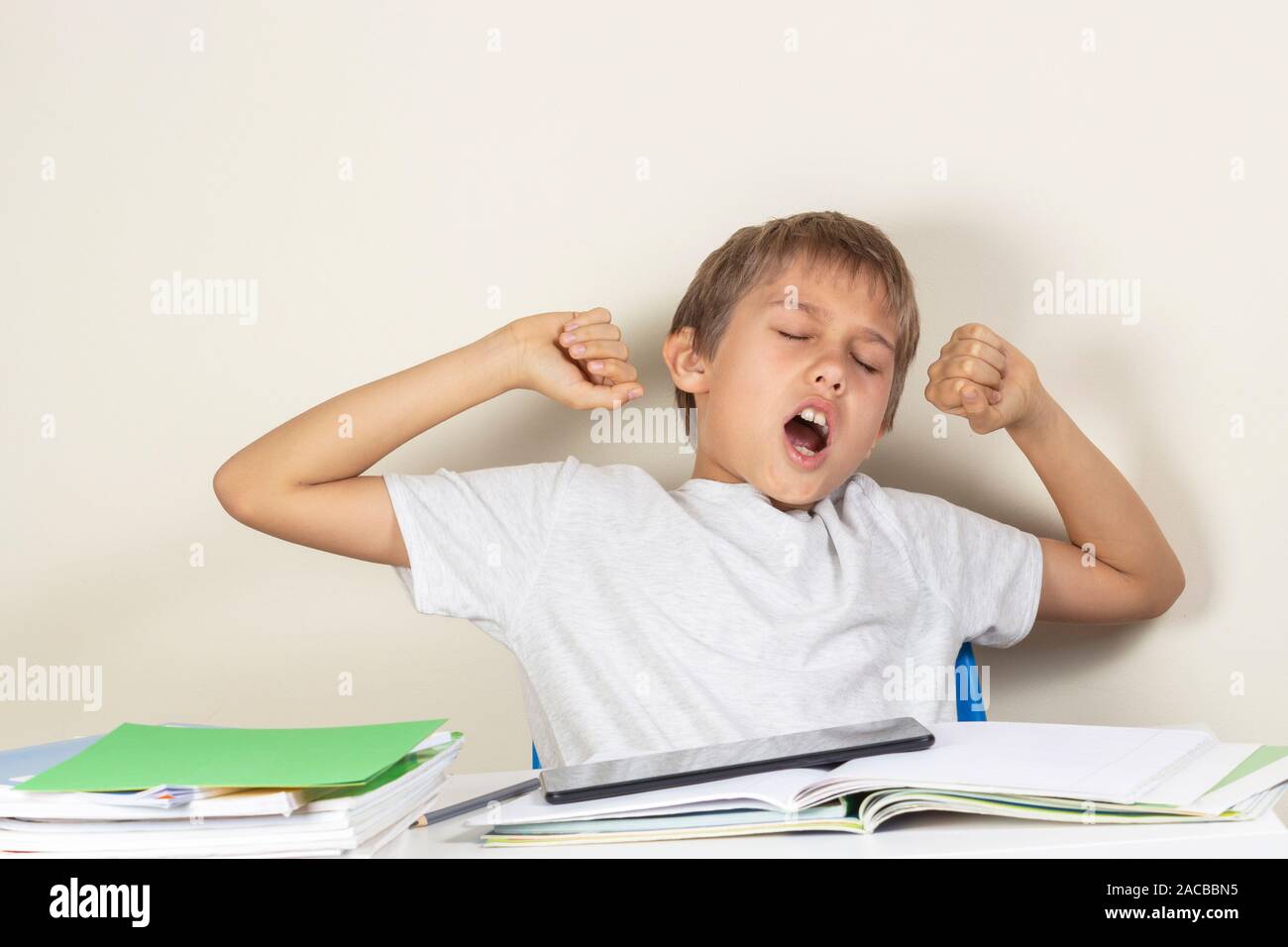 Tired kid yawning when making homework with books, notebooks and digital tablet Stock Photo