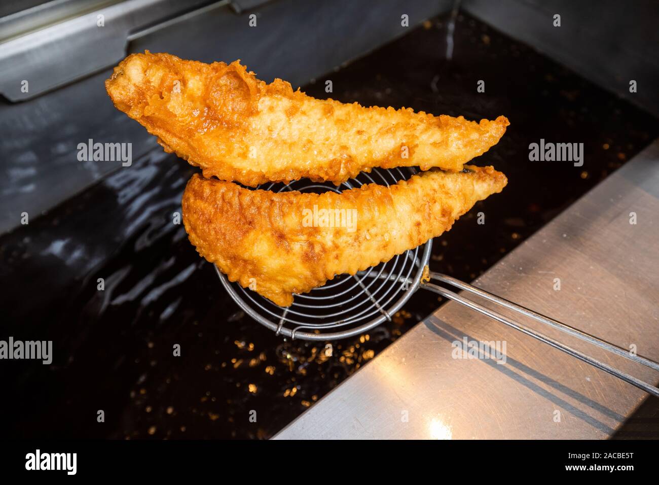 Cooked and battered fish being taken out of in a deep fat fryer in a