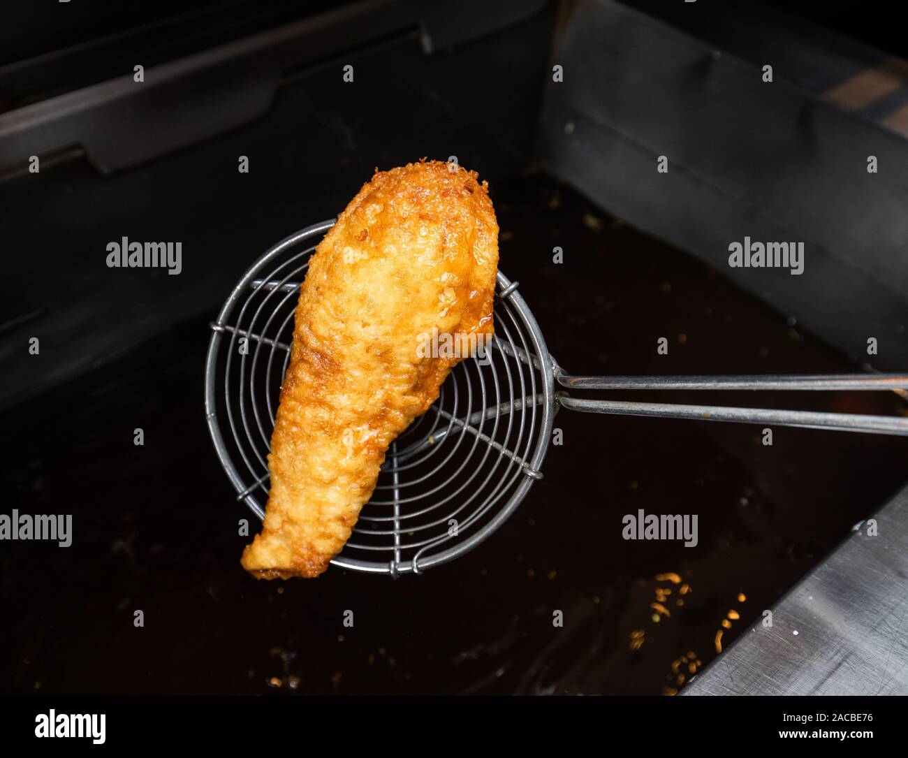 Cooked and battered fish being taken out of in a deep fat fryer in a