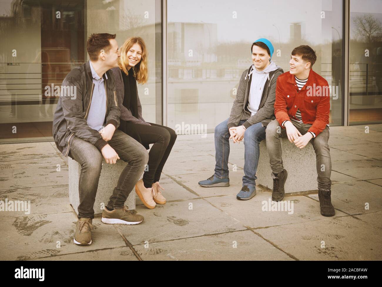 group of young teenage friends talking and laughing together - candid real people with vintage filter Stock Photo