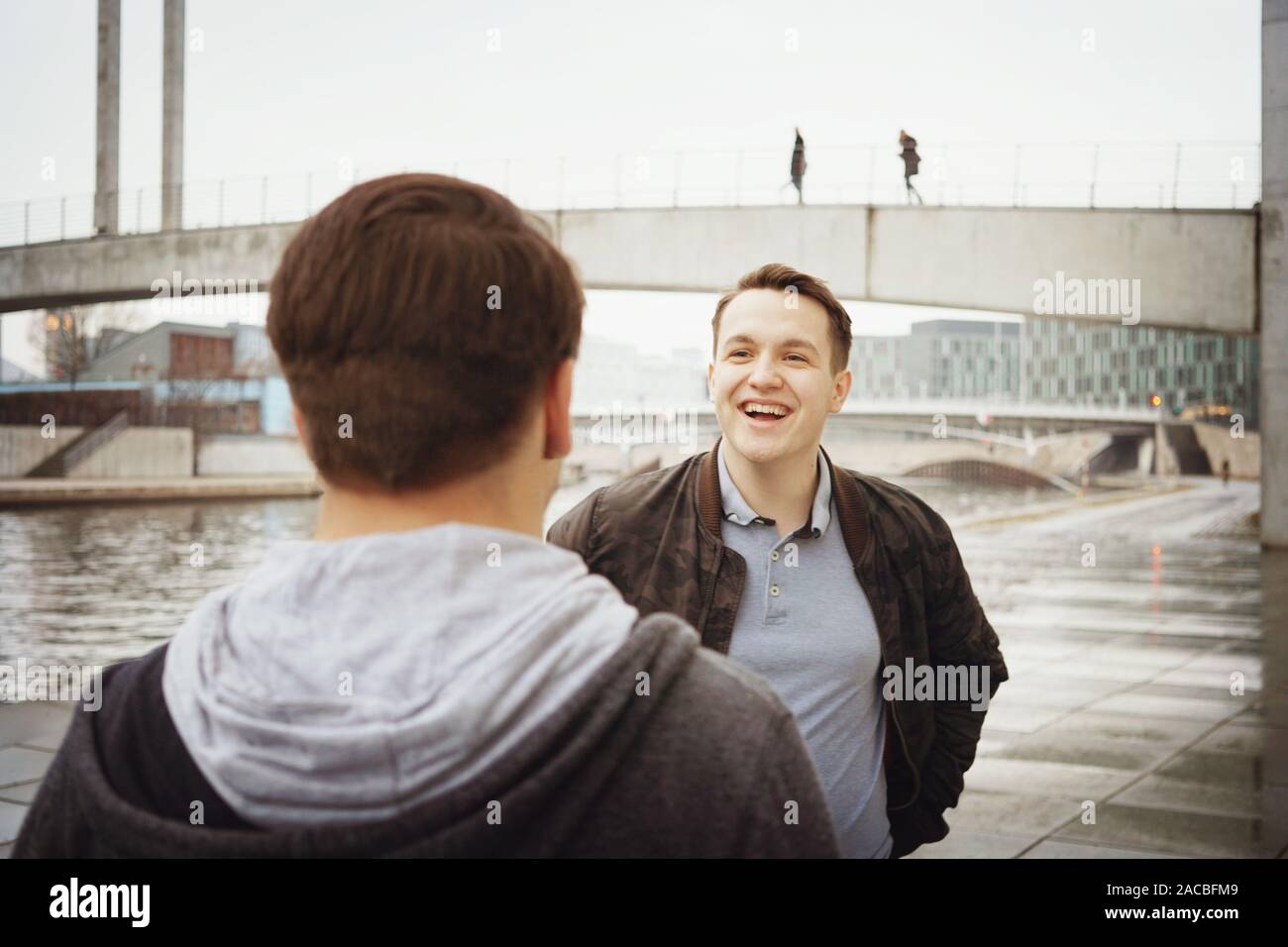two male teenage friends having a fun conversation - lifestyle or city life concept - urban riverside location in Berlin Germany Stock Photo
