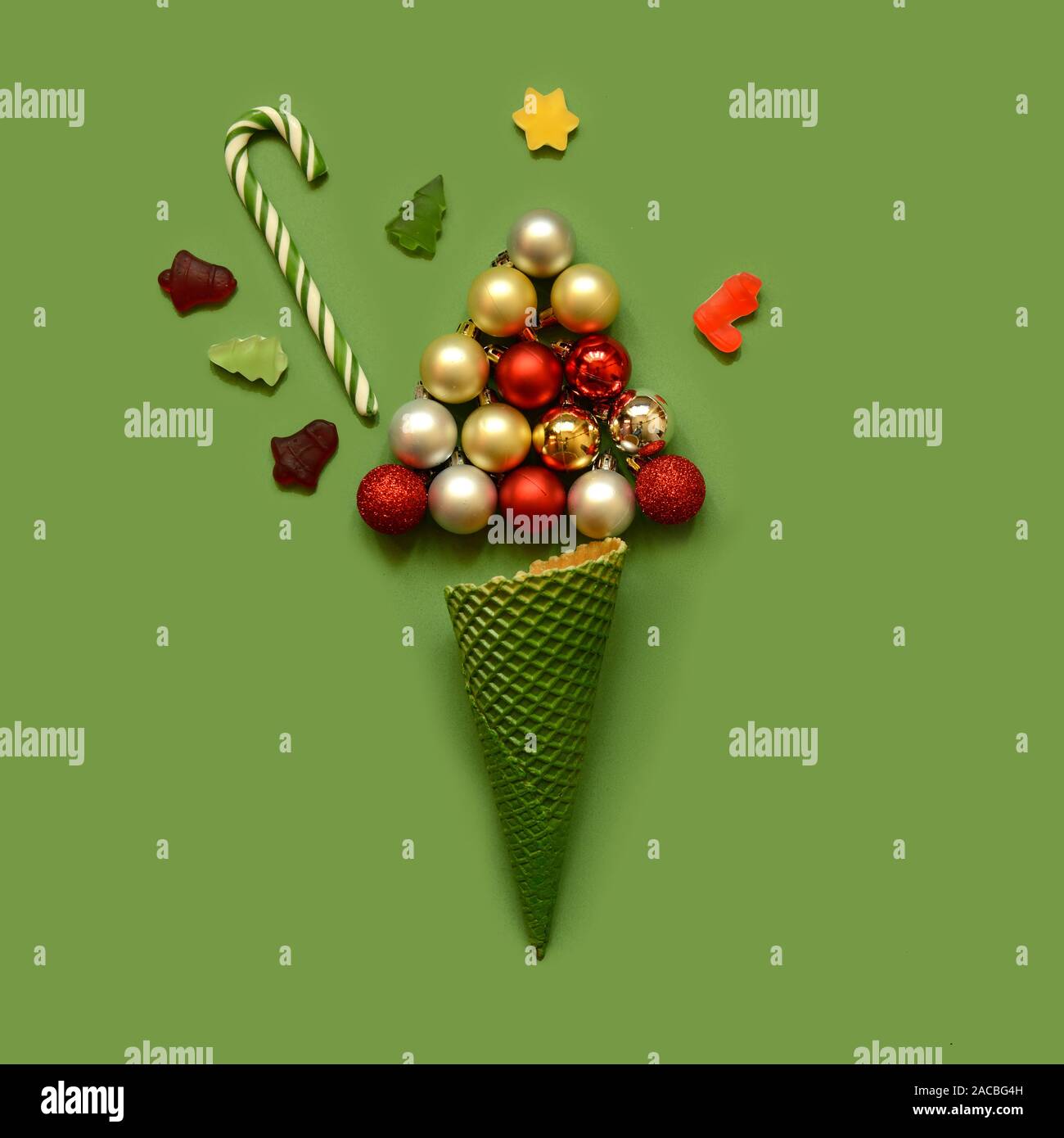 Christmas composition. Ice cream waffle cone with tree from balls,candy canes and sweets on green background. Christmas, winter, new year concept. Fla Stock Photo