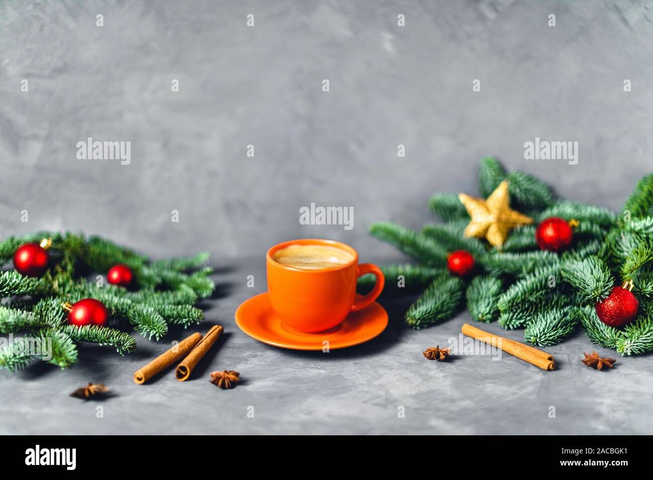 Christmas and New year composition with orange cup of coffee surrounded by fir brunches with red balls on gray table. Stock Photo