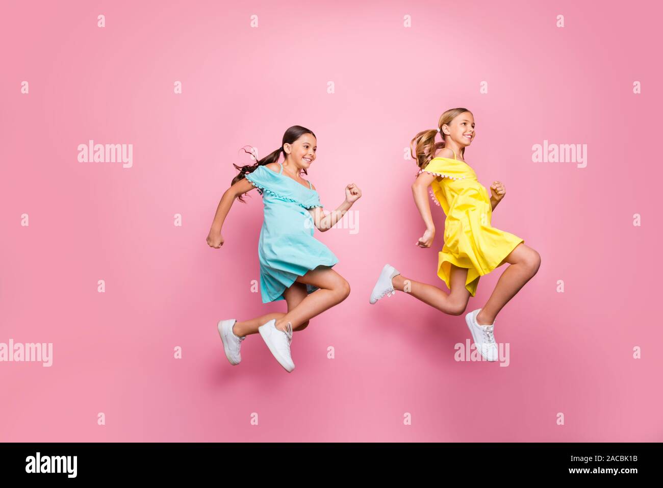 Full body profile photo of two friendship small ladies models jumping high hurry home summer holidays begin wear blue yellow dresses isolated pink Stock Photo