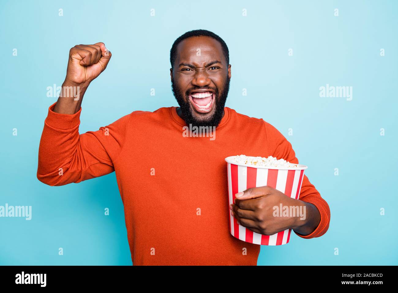 Photo of cheerful overjoyed ecstatic crazy man screaming in happiness  holding pop corn bucket with emotional facial expression in orange sweater  Stock Photo - Alamy