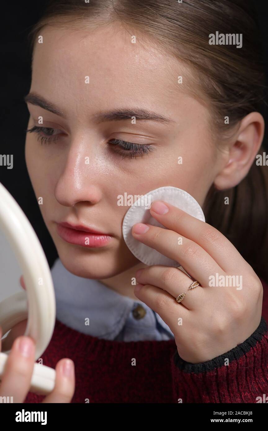 Girl Wipes Her Face With A Cotton Pad in Mirror Stock Photo