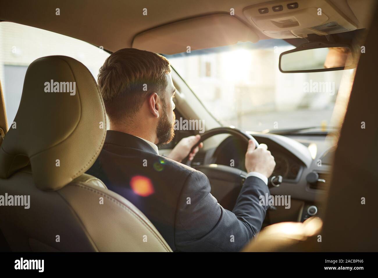 Rear view of young bearded man holding wheel and looking through the windshield and driving Stock Photo