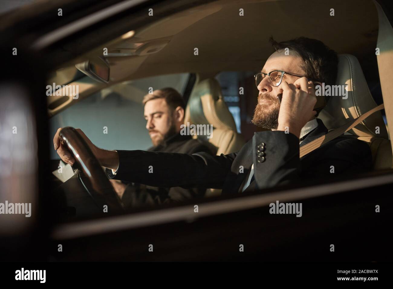 Young bearded driver in eyeglasses using his mobile phone during ...