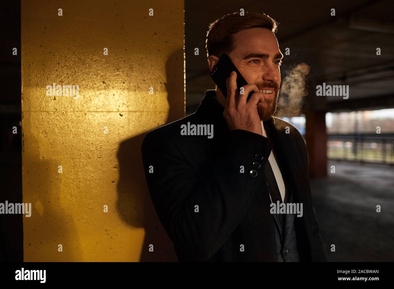 Smiling young bearded man has a conversation on mobile phone while standing in the underground parking Stock Photo