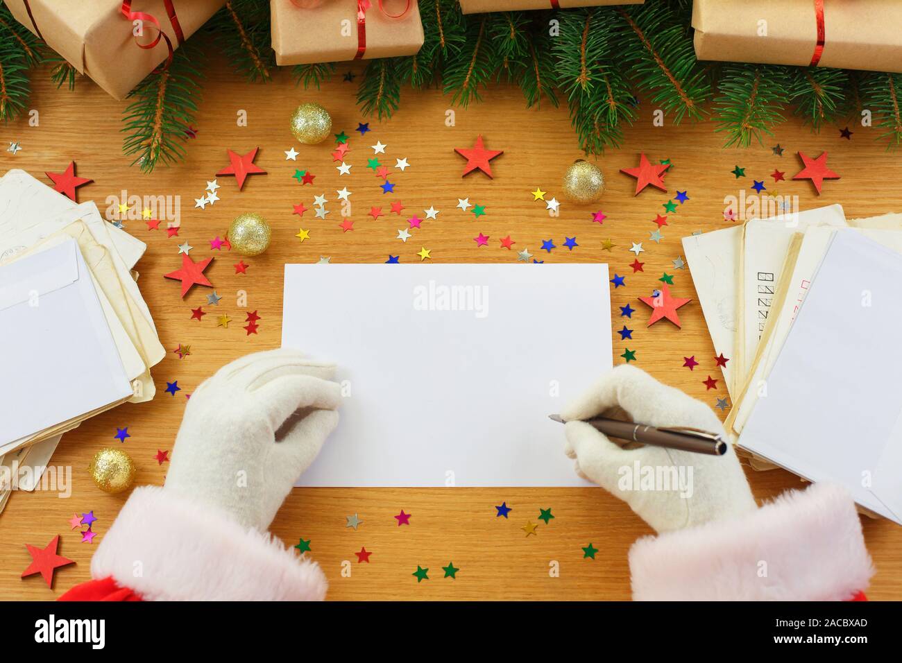 Santa Claus writing Christmas letter or wish list around gift boxes, Christmas tree and many envelopes. mockup blank. christmas greetings Stock Photo