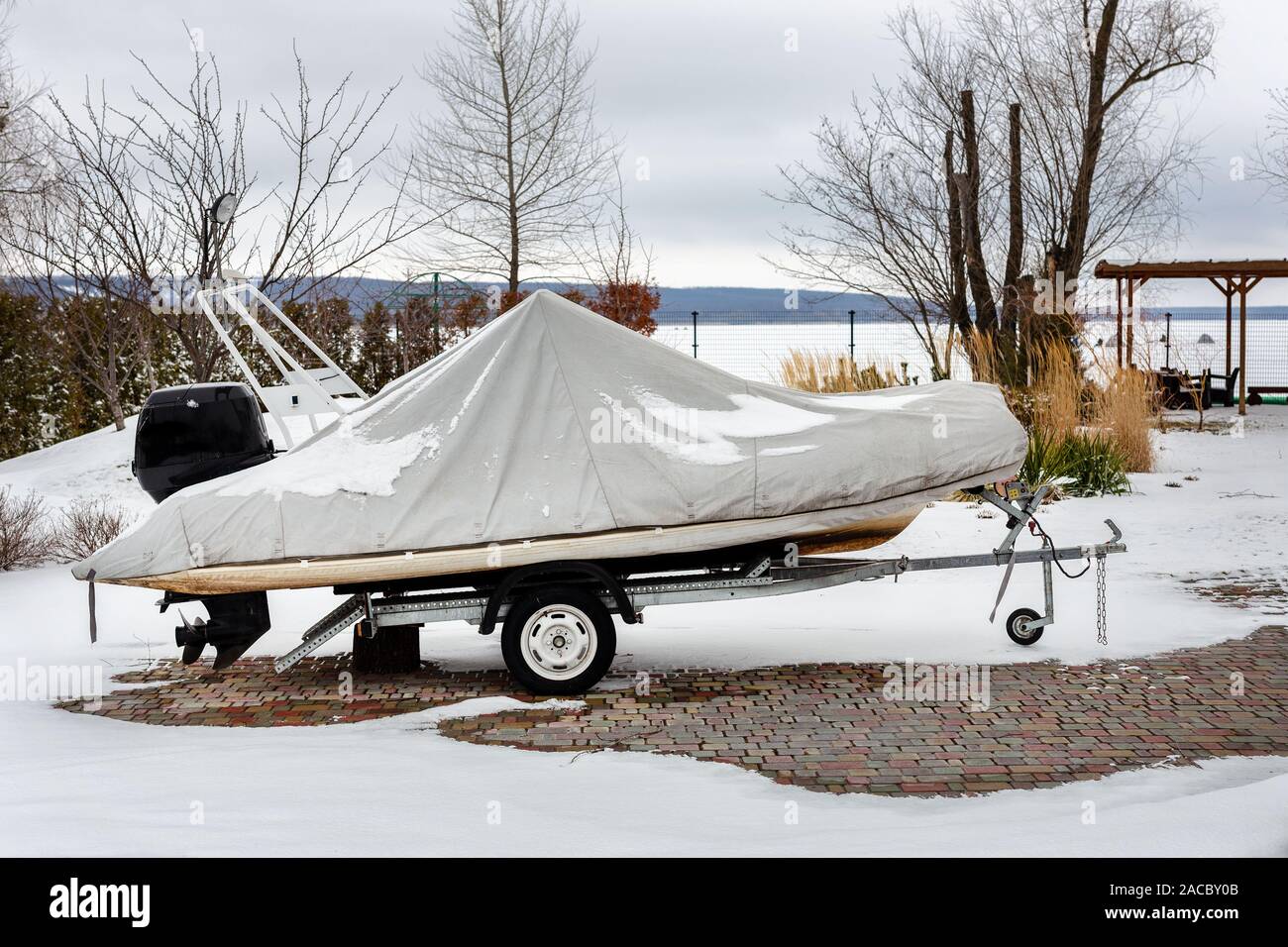 Inflatable luxury fishing motorboat wrapped in cover standing over trailer for winter period