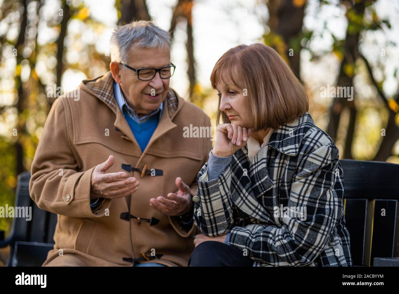 Senior couple is sitting on bench in park and talking. Stock Photo