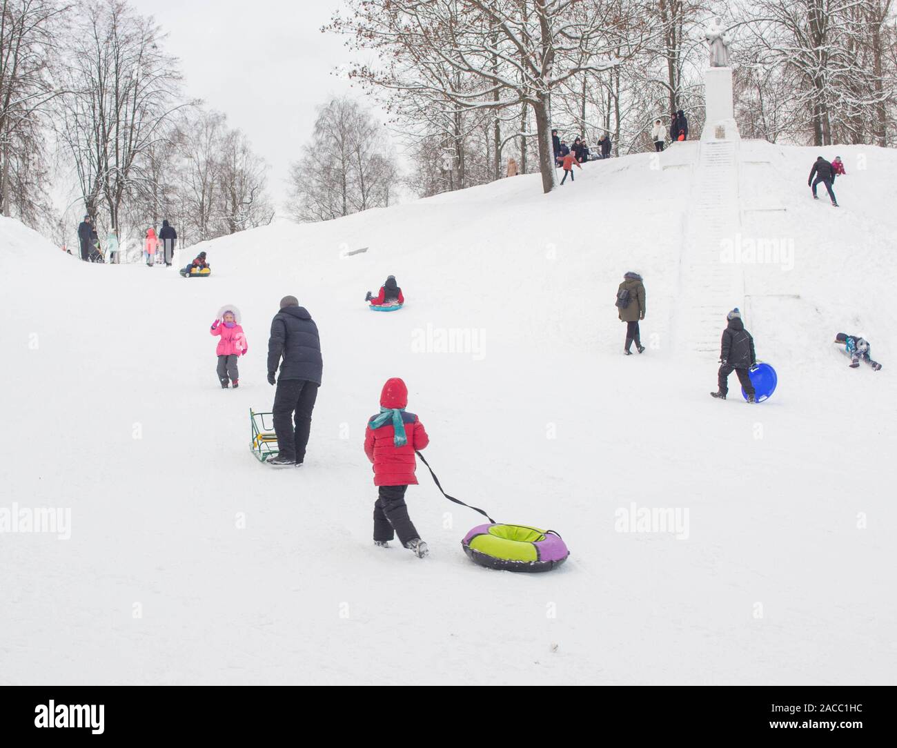 A lot of people children and adults ride a sled in the winter in the snow, gladness. BOBRUISK, BELARUS - 03.01.19 Stock Photo