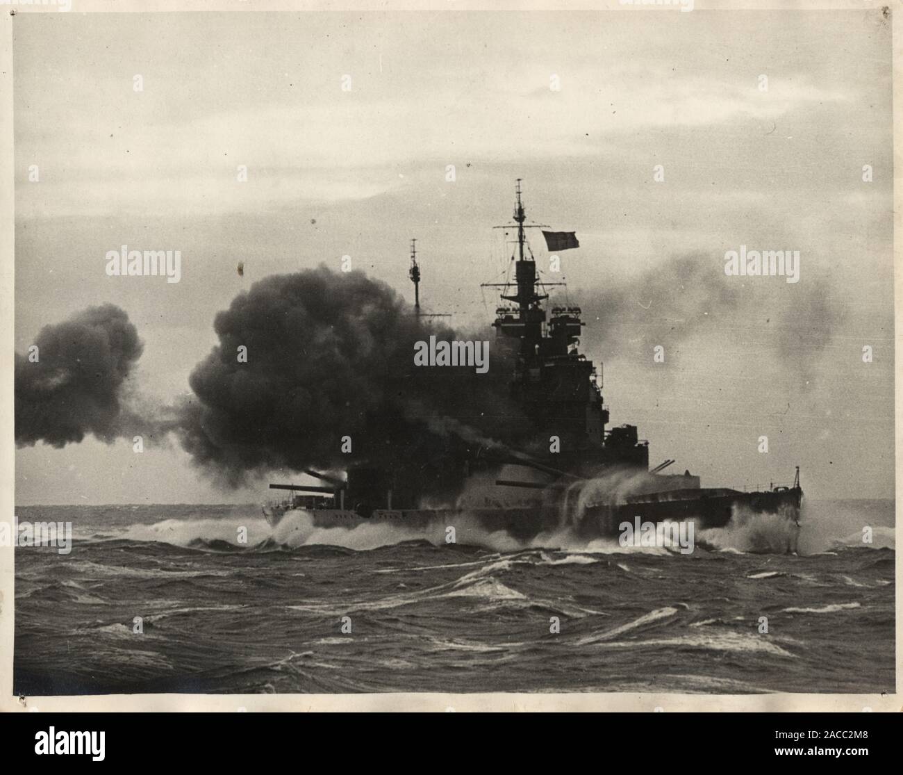 Vintage photograph of a Broadside firing by HMS Duke of York Royal Navy Battleship. HMS Duke of York was a King George V class battleship of the Royal Navy. Commissioned into the Royal Navy on 4 November 1941, subsequently seeing combat service during the Second World War. Stock Photo