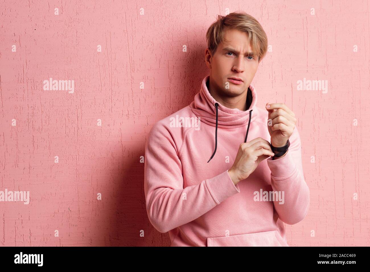 Friendly blond student guy in pink hoodie on pink background, copy space. Portrait of a young man in informal clothes, positive as a lifestyle. Stock Photo