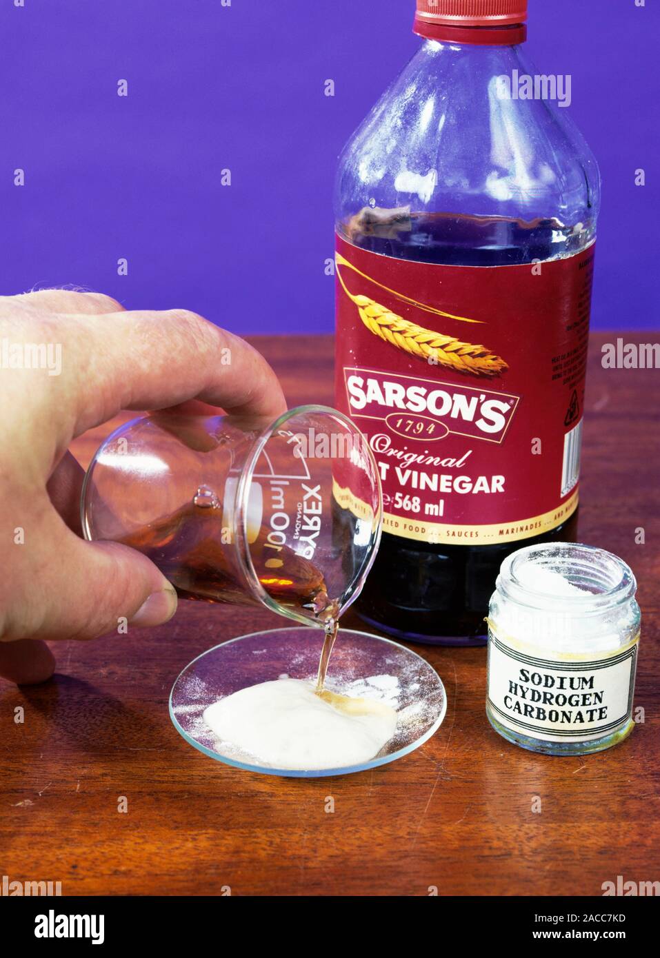 Chemistry experiment. Hand pouring vinegar onto baking soda (sodium