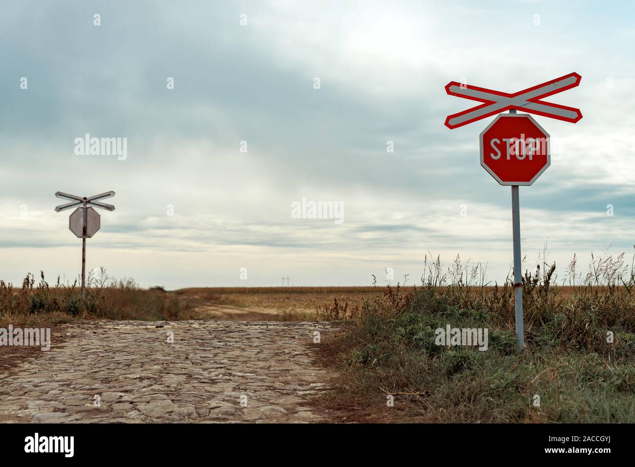 St Andrew's Cross and stop sign at railroad level crossing and country cobblestone road junction Stock Photo