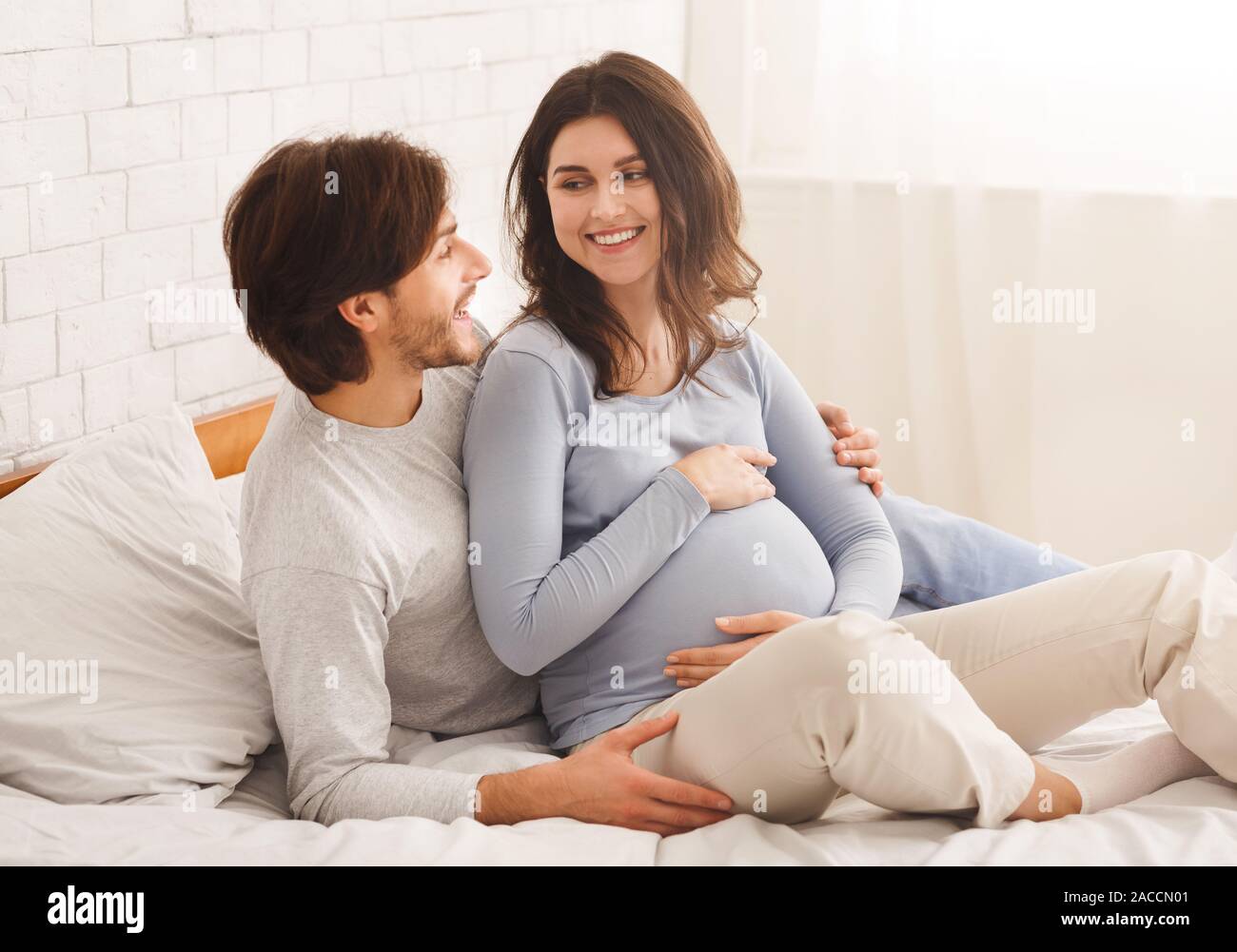 Happy pregnant couple relaxing on bed at home together Stock Photo