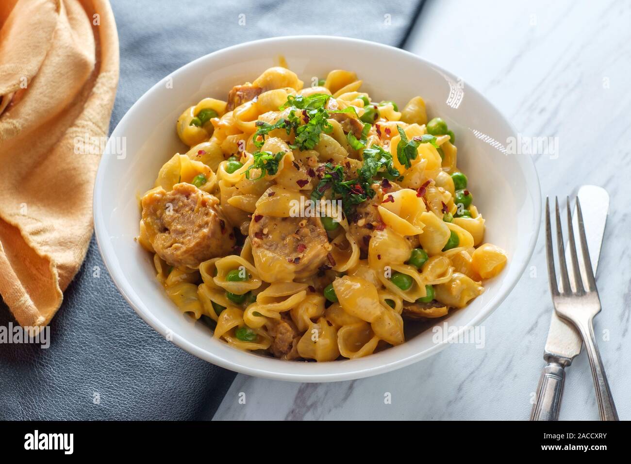 Sausage macaroni and cheese with green peas in bowl on marble kitchen table Stock Photo