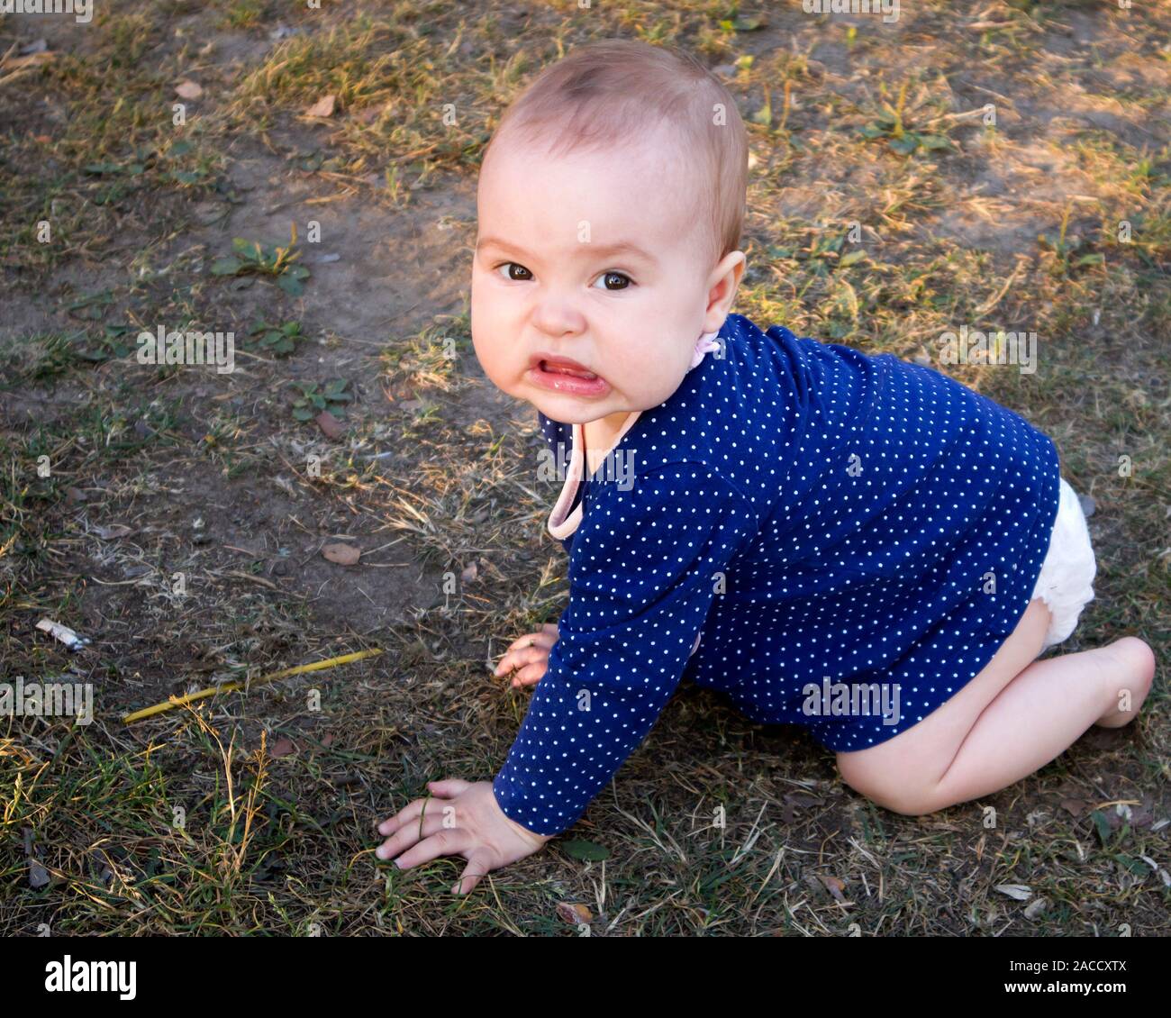 Adorable infant girl trying to make her first steps and grimacing at the camera Stock Photo
