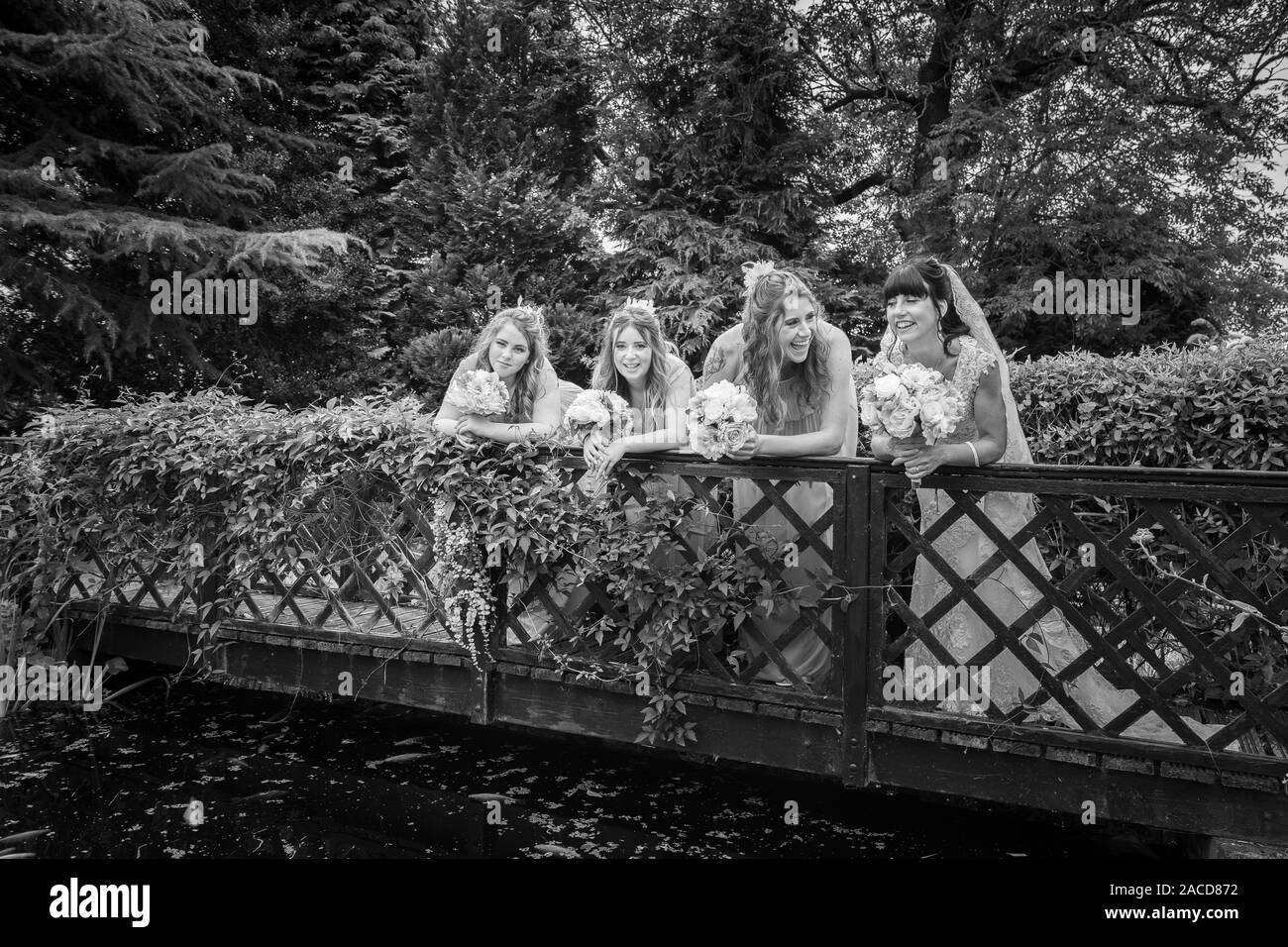 A stunning bride and her bridesmaids standing on a ornate bridge laughing, smiling while having Wedding pictures taken at the Manor Hotel in Cheadle Stock Photo