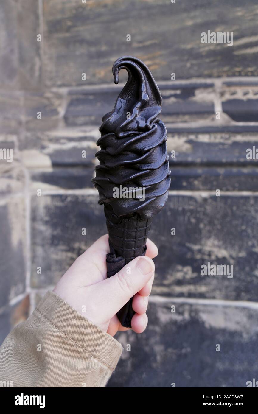 hand holding black soft serve ice cream cone made with activated charcoal Stock Photo
