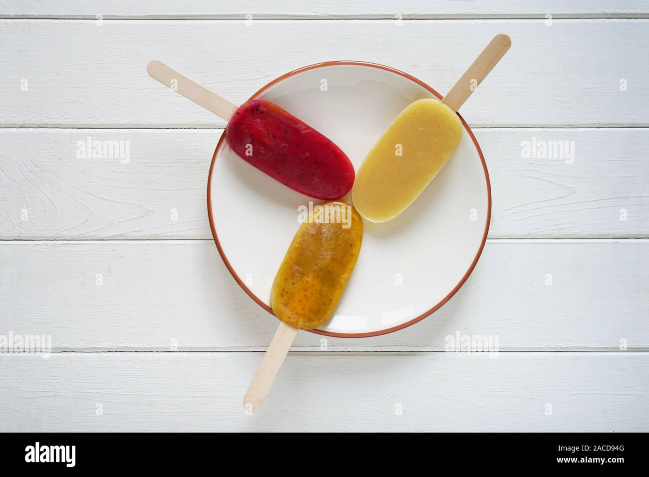 overhead view of three different fruit smoothie popsicles or ice pops on a plate on white wooden background Stock Photo