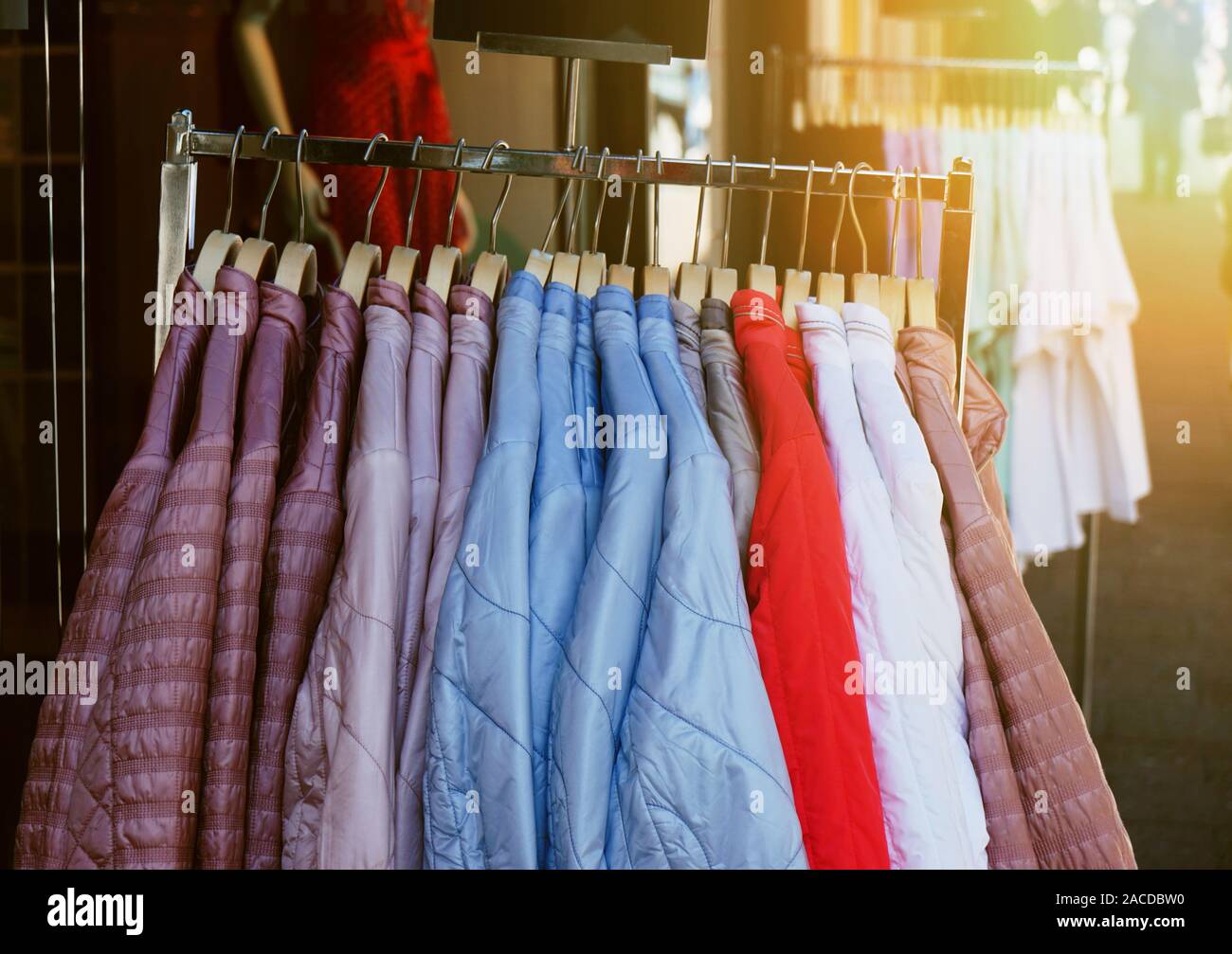 clothes rack with ladieswear spring fashion jackets hanging outside store - trendy filter with sun flare light leak Stock Photo