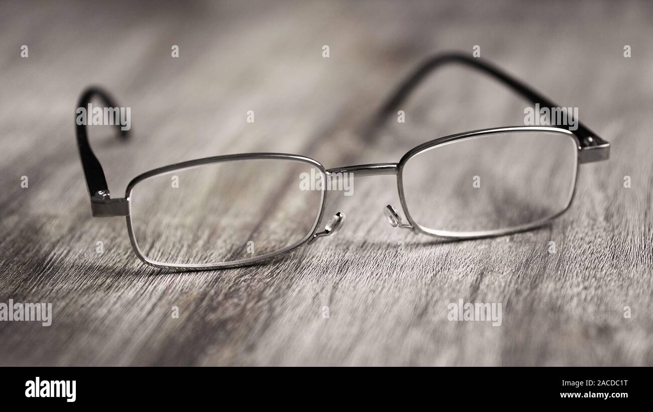Pair of modern reading glasses or spectacles on rustic wooden table - selective focus with shallow deph of field Stock Photo