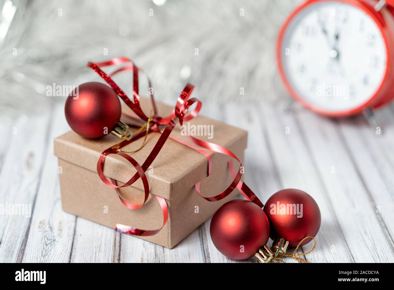 Gift box and blurred alarm clock on background on a wooden table decorated with a garland and red Christmas balls for the New Year or XMAS. Copy space Stock Photo