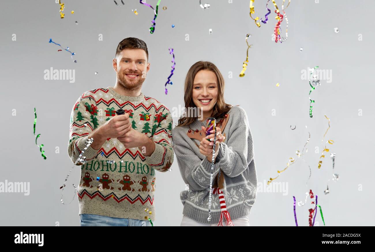 couple in christmas sweaters popping party poppers Stock Photo