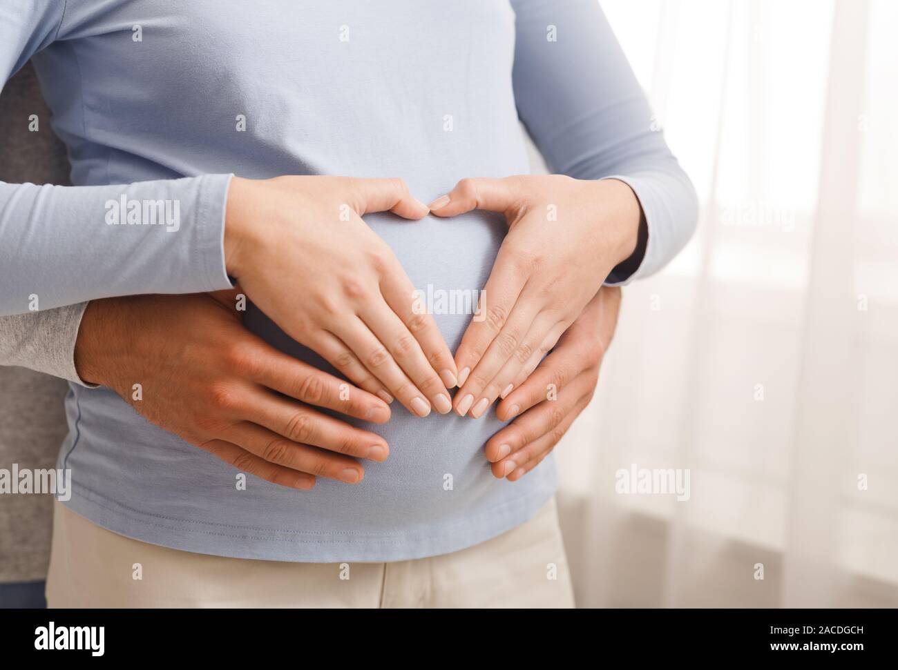 Loving couple making heart shape of their hands on pregnant belly Stock