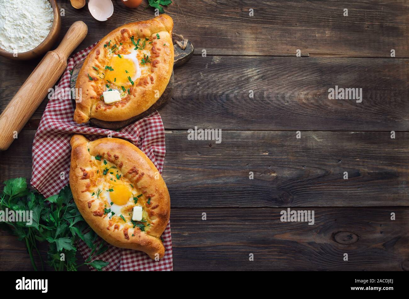 Fresh homemade khachapuri Ajarian on rustic wooden background. Dough boats filled with sulguni cheese and egg. Traditional Georgian cuisine. Top view. Stock Photo