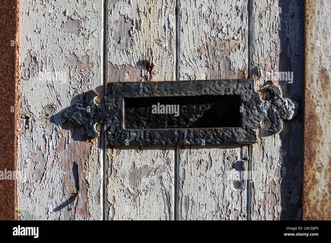 Weathered wooden door with peeling paint and an old black letter box, UK Stock Photo