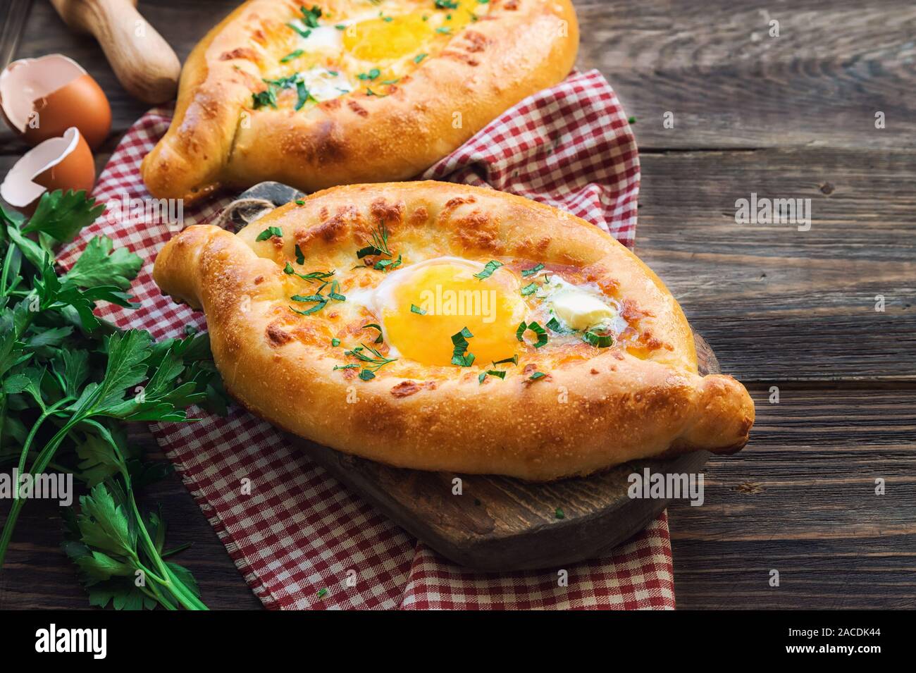 Fresh homemade khachapuri Ajarian on rustic wooden background. Dough boats filled with sulguni cheese and egg. Traditional Georgian cuisine. Stock Photo