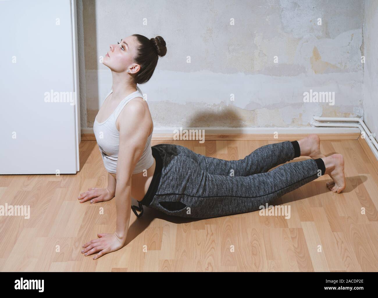sporty young woman performing yoga stretching exercise on the floor at home - Bhujangasana or cobra pose Stock Photo
