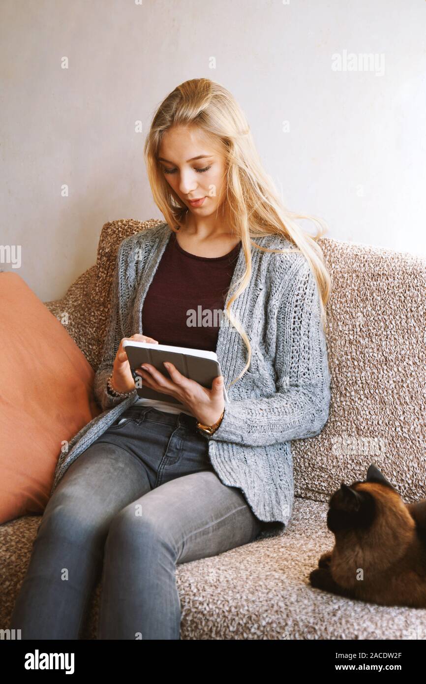teenage girl using tablet computer at home while relaxing on sofa with cat - candid real people lifestyle Stock Photo